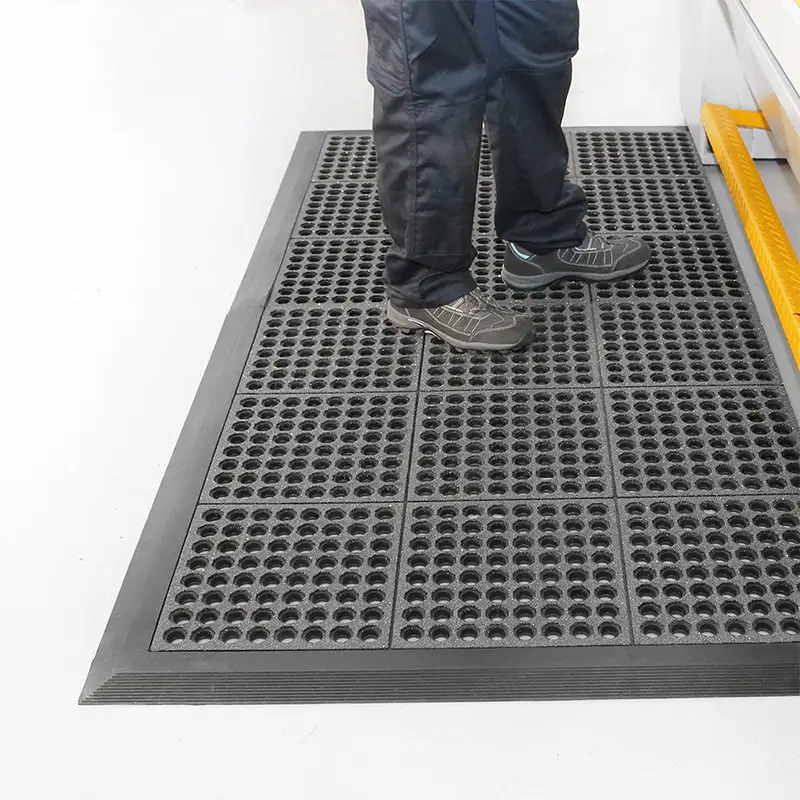 Industrijski otirači Steep – radnik stoji na crnom modularnom otiraču sa crnim ivicama uz industrijsku mašinu