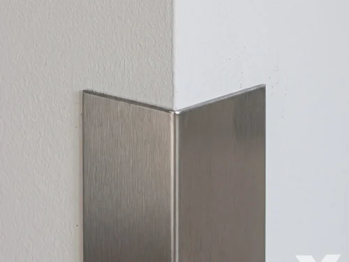 Detalj brušenog inox profila sa dva kraka koji prekrivaju spoljni ugao belog zida